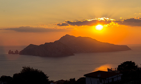 The sun sets dramatically behind an island on a Capri yacht charter